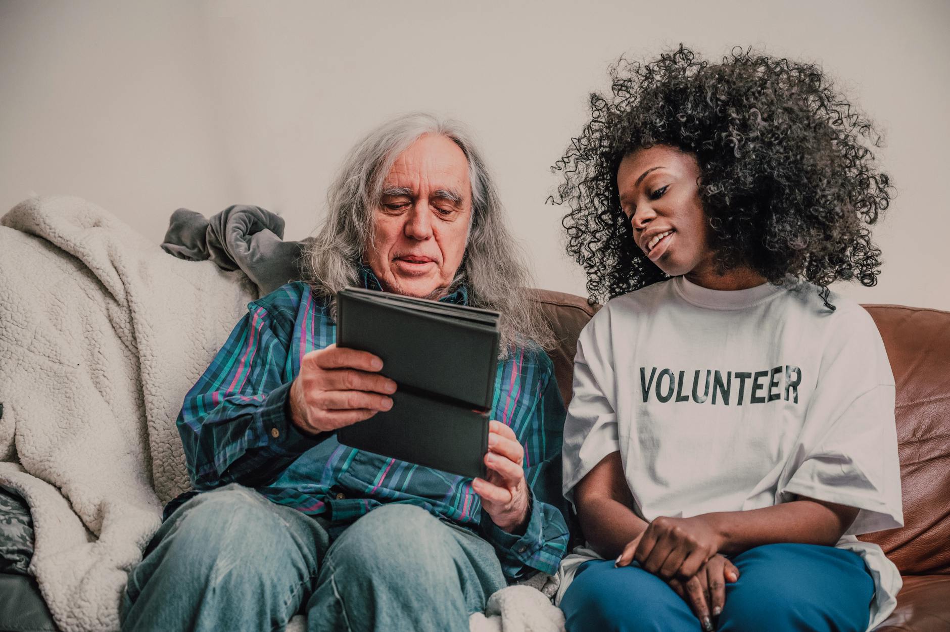 a woman wearing volunteer shirt sitting beside elderly man holding tablet computer