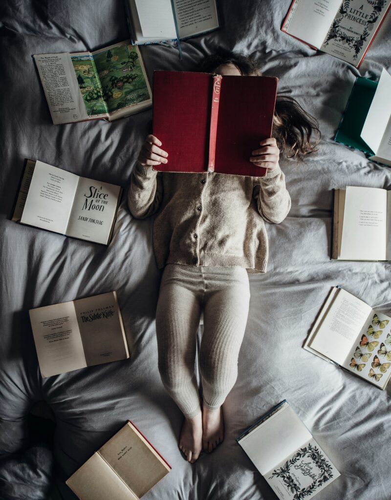 a young girl reading books on a bed